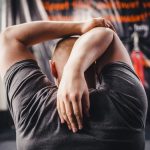 Man stretching arms in a gym, viewed from behind, focusing on fitness and flexibility.